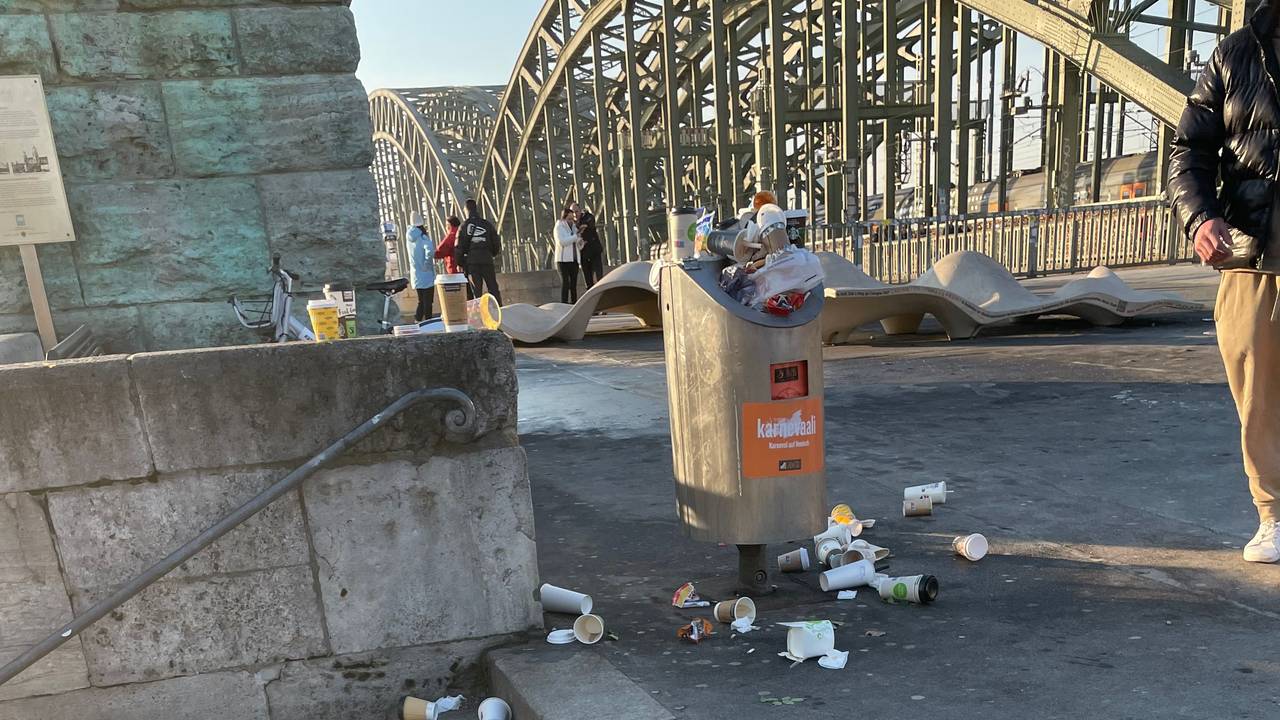 Um einen Mülleimer herum liegen To-Go-Becher auf dem Boden und auf den Stufen einer angrenzenden Treppe.