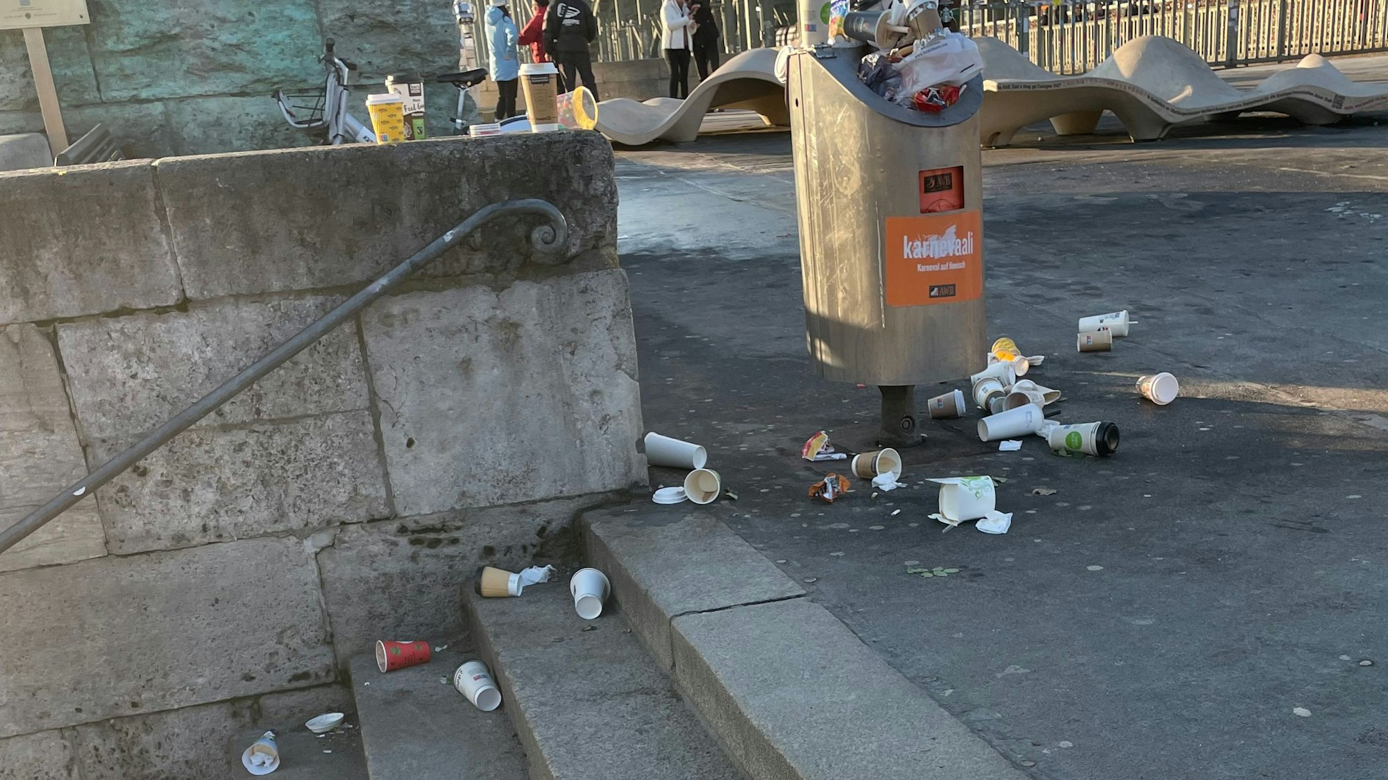 Um einen Mülleimer herum liegen To-Go-Becher auf dem Boden und auf den Stufen einer angrenzenden Treppe.