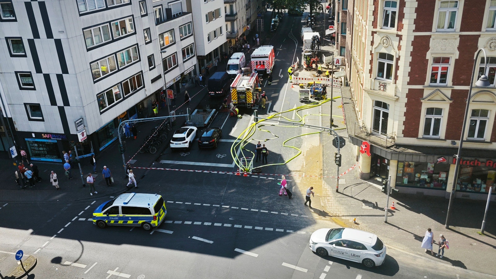 Einsatzfahrzeuge stehen auf einer Straße, auf der Fahrbahn sind mehrere Schläuche.