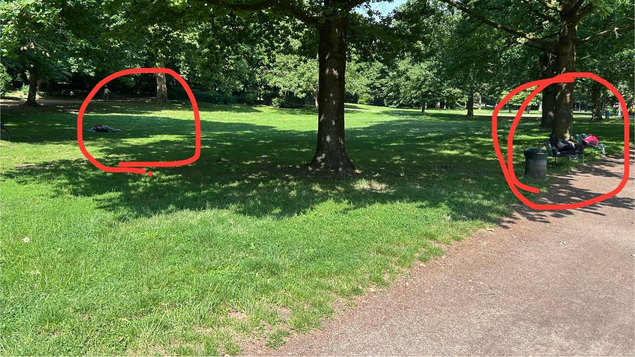 Im Volksgarten liegt ein Mann ausgestreckt auf einer Parkbank, ein anderer auf dem Rasen.