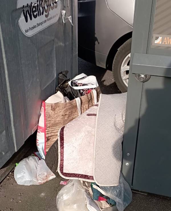 Zwischen zwei Containern stehen gefüllt Plastiktüten, darüber liegt ein Teppich.
