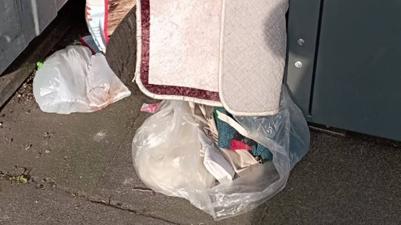 Zwischen zwei Containern stehen gefüllt Plastiktüten, darüber liegt ein Teppich.