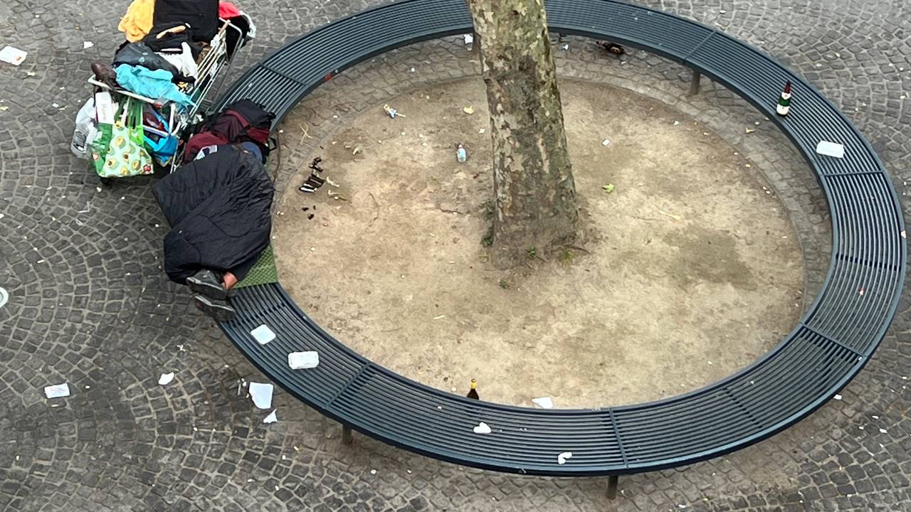 Eine Person liegt zusammengerollt auf einer Bank.