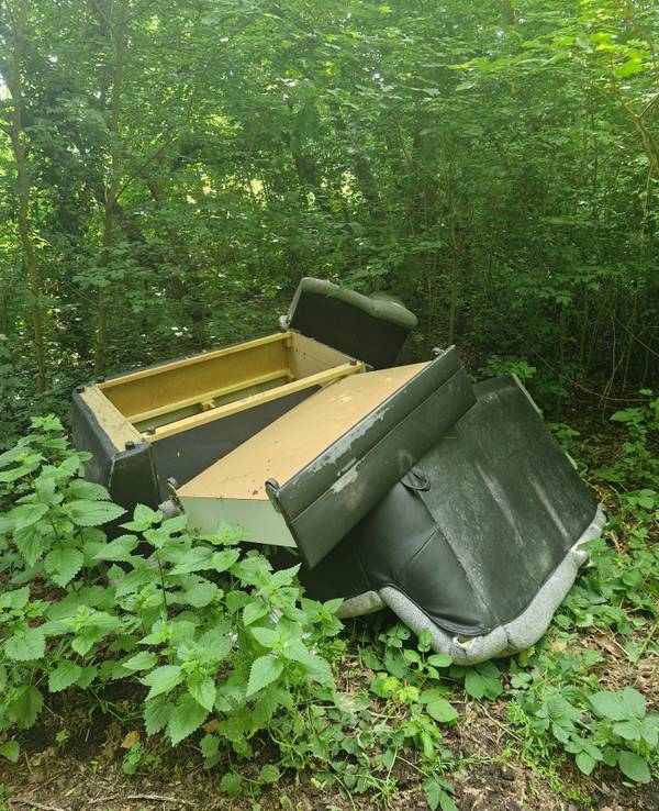 Ein Kunstleder-Sofa liegt in mehreren Teilen in einem Gebüsch.