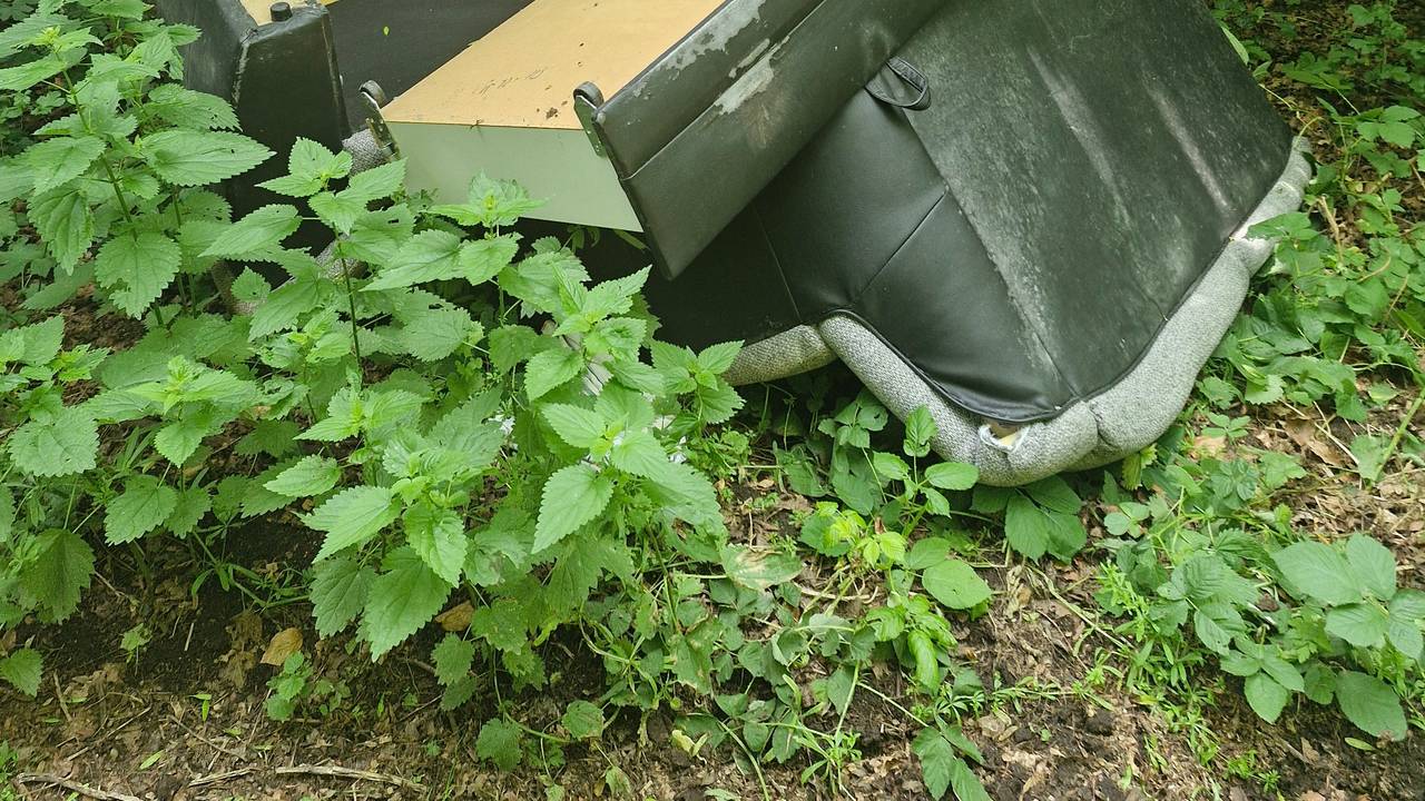 Ein Kunstleder-Sofa liegt in mehreren Teilen in einem Gebüsch.