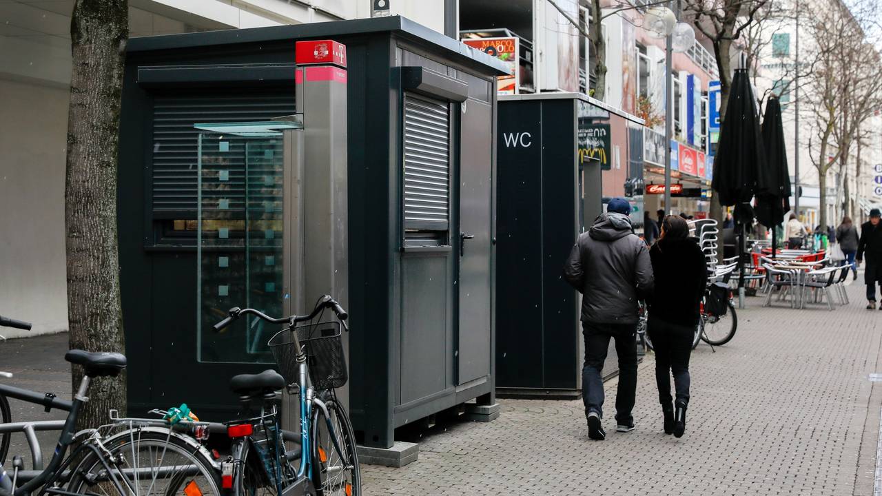Vor einem Toilettenhäuschen mit WC-Aufschrift steht ein weiterer Container, dieser hat jedoch ein großes Fenster.