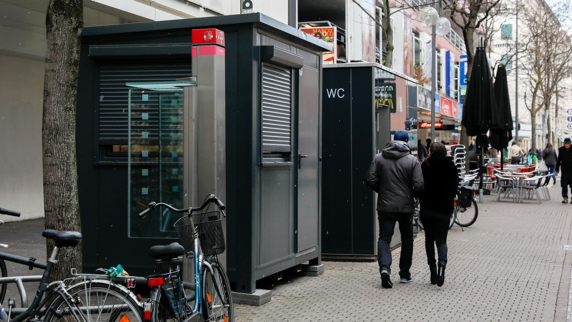 Vor einem Toilettenhäuschen mit WC-Aufschrift steht ein weiterer Container, dieser hat jedoch ein großes Fenster.