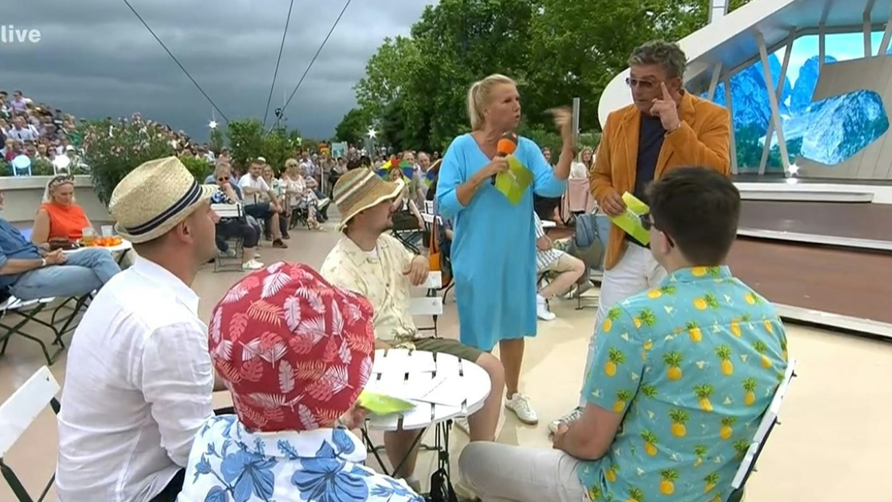 ZDF-Fernsehgarten-Moderatorin Andrea Kiewel und der „Bergdoktor“ Hans Sigl – im Hintergrund sind dunkle Wolken zu sehen.