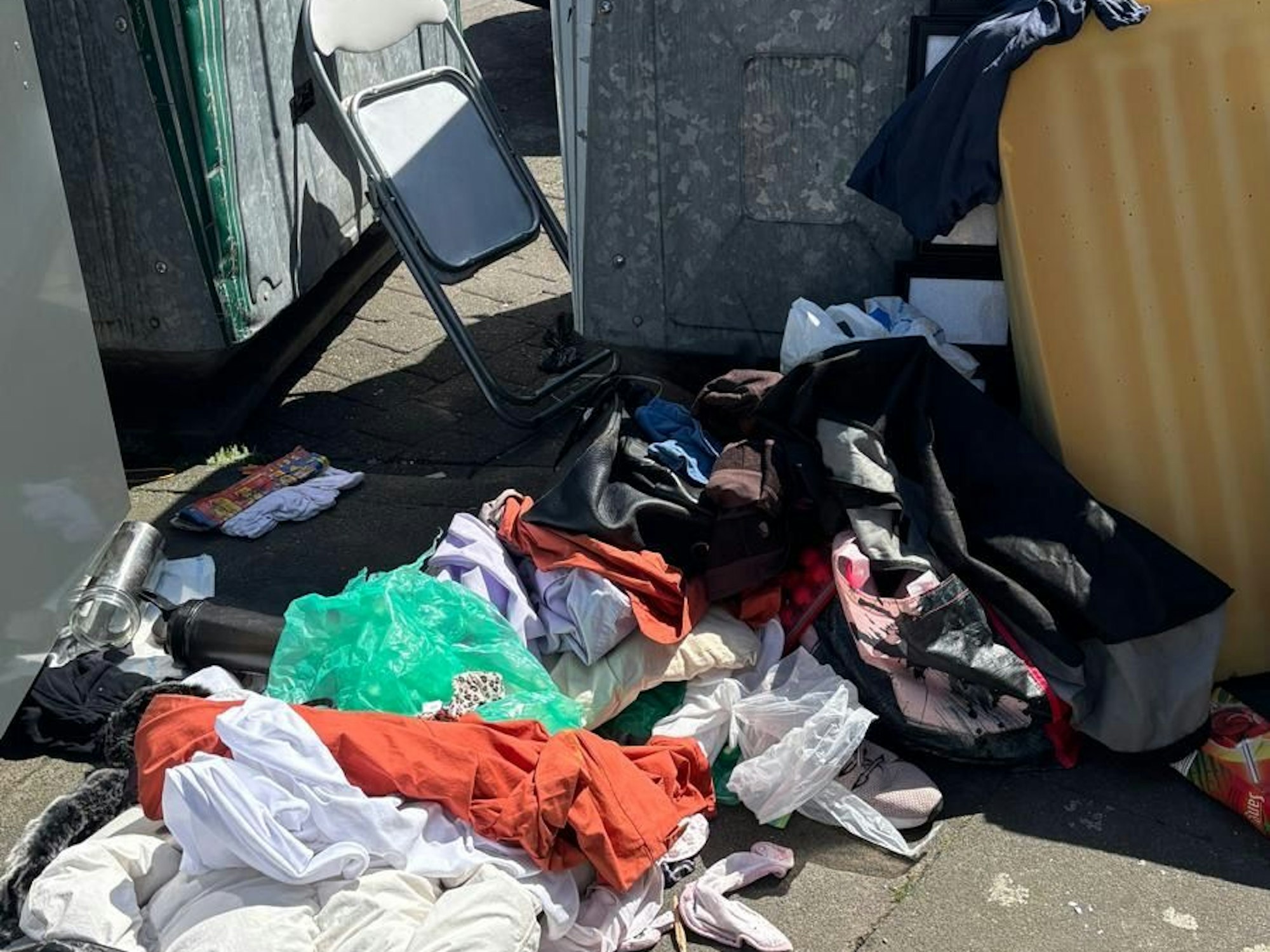 Vor Müllcontainern liegen Kleidungsstücke, steht eine alte Matratze.