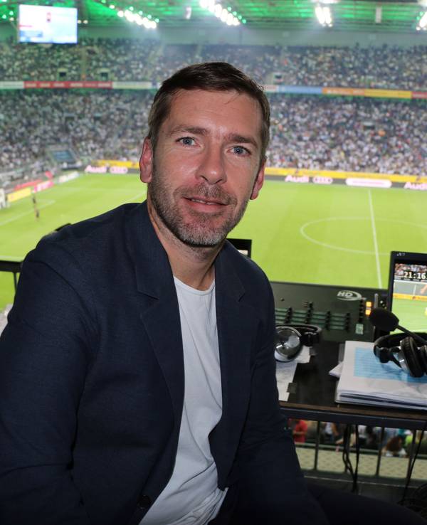 Marco Hagemann sitzt im Stadion an seinem Kommentatoren-Platz und posiert für ein Foto.