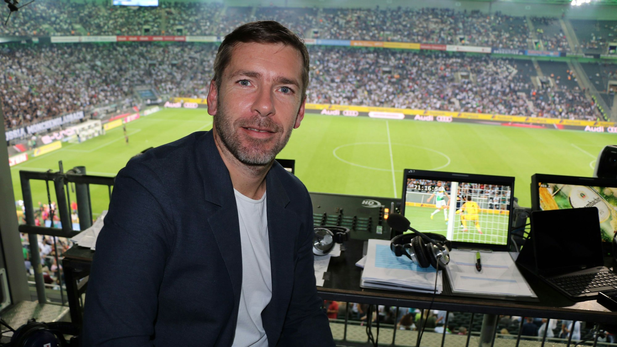 Marco Hagemann sitzt im Stadion an seinem Kommentatoren-Platz und posiert für ein Foto.