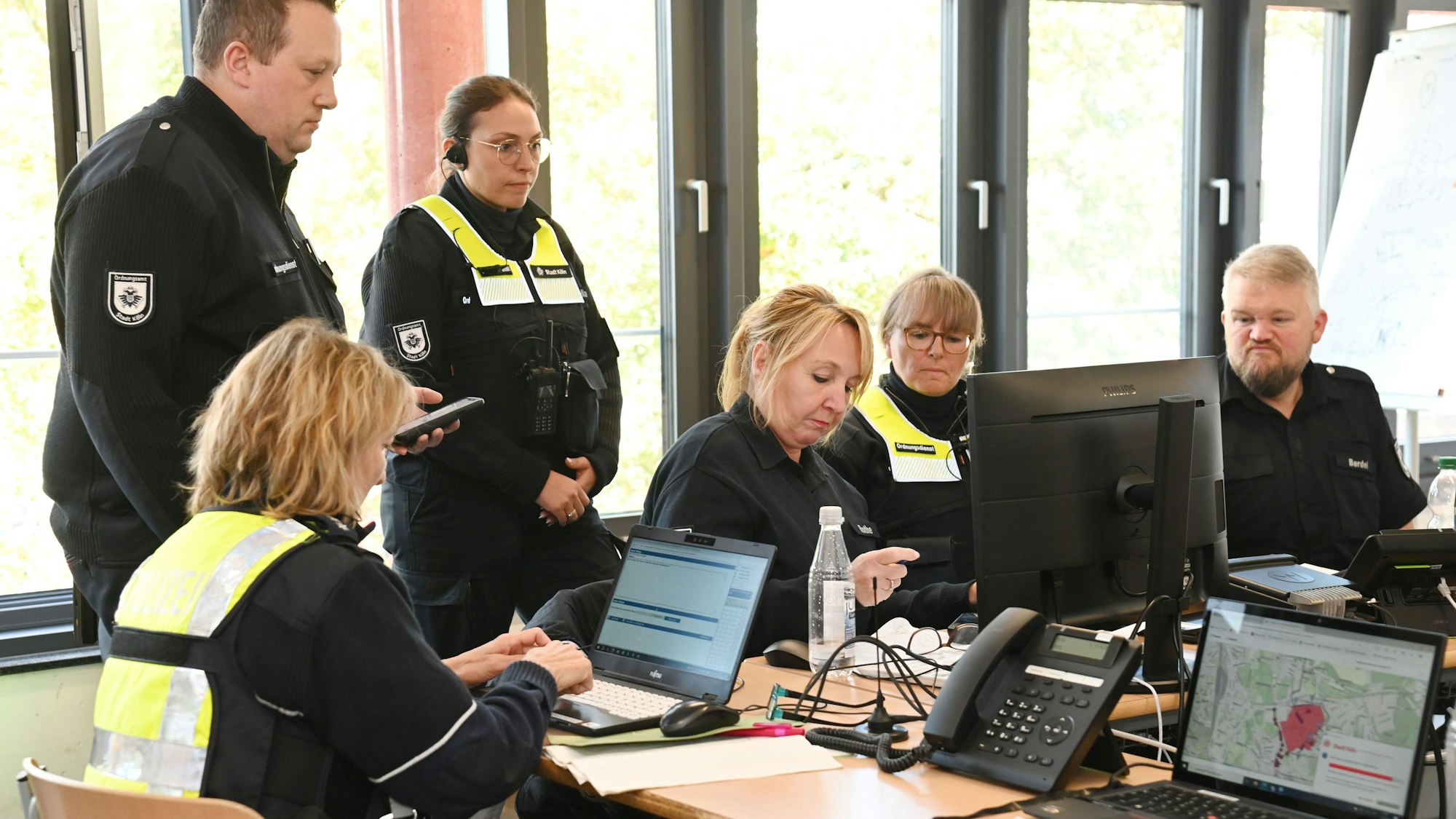 Einsatzkräfte sitzen vor Computern, zwei stehen.