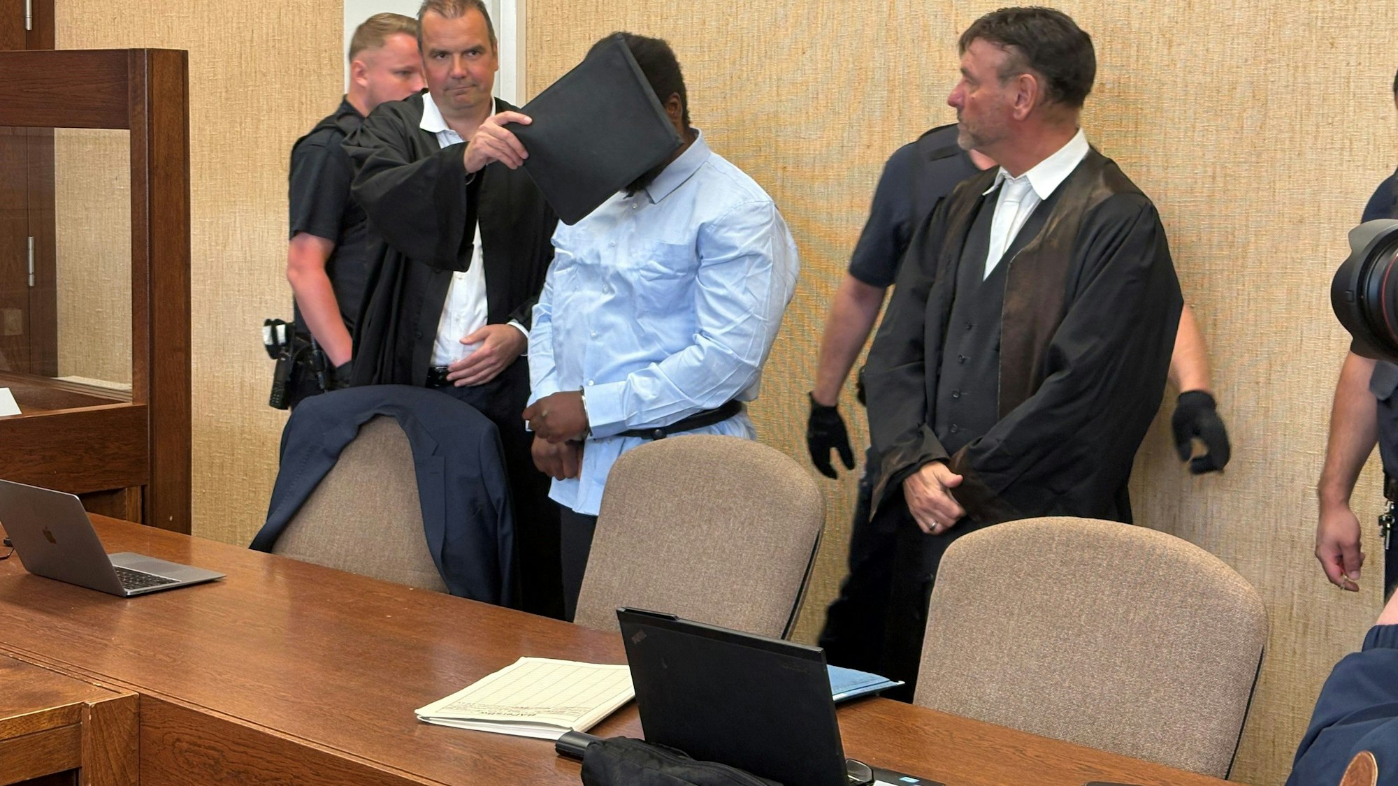 Der Angeklagte, hier mit seinen Verteidigern, soll einer Polizistin ein Stück vom Ohr abgebissen haben.