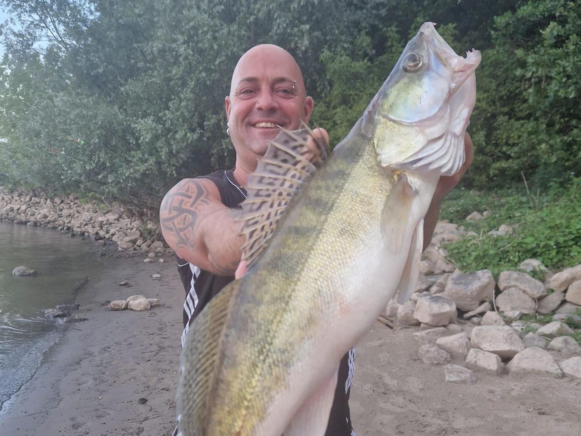Ein Mann hält einen großen Fisch vor seinen Körper.