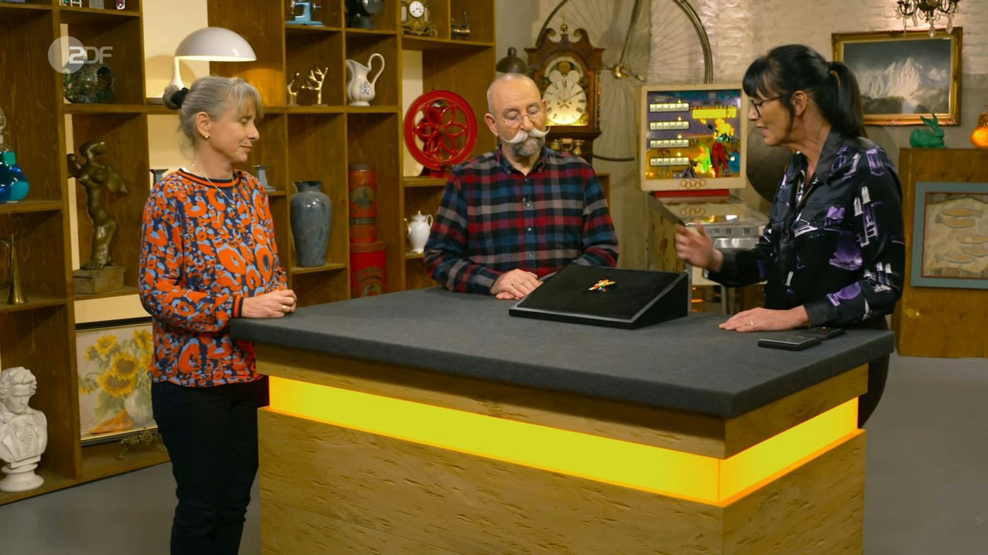 Eine Brosche nach Niki de Saint Phalle war am Donnerstag das Highlight bei „Bares für Rares“, von links: Verkäuferin Heike, Moderator Horst Lichter und Expertin Heide Rezepa-Zabel. (Bild: ZDF)