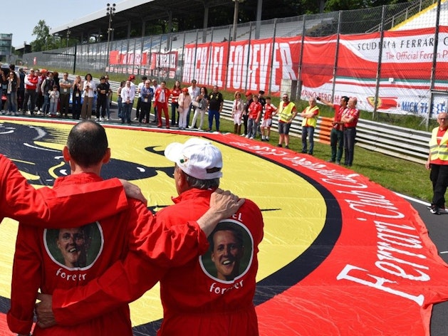 Ferrari-Besitzer erinnern in Monza mit einer Riesen-Fahne und Overalls mit der Aufschrift ‚Michael forever‘ an Rekordweltmeister Michael Schumacher.