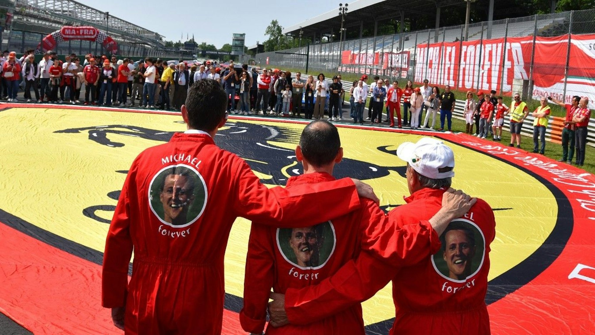 Ferrari-Besitzer erinnern in Monza mit einer Riesen-Fahne und Overalls mit der Aufschrift ‚Michael forever‘ an Rekordweltmeister Michael Schumacher.