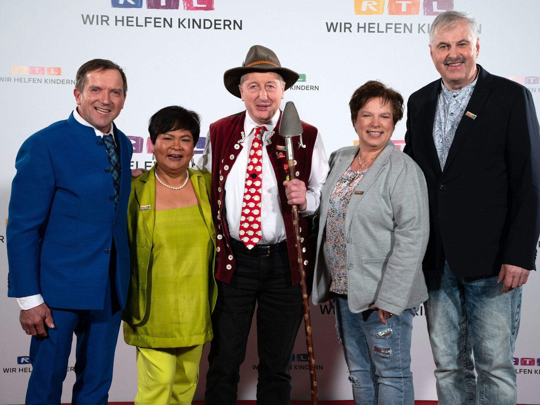 Beim RTL-Spendenmarathon stehen in Köln die fünf Protagonisten von „Bauer sucht Frau“ (Josef, Narumol, Schäfer Heinrich, Anja und Bruno) vor einer Werbewand und lächeln.