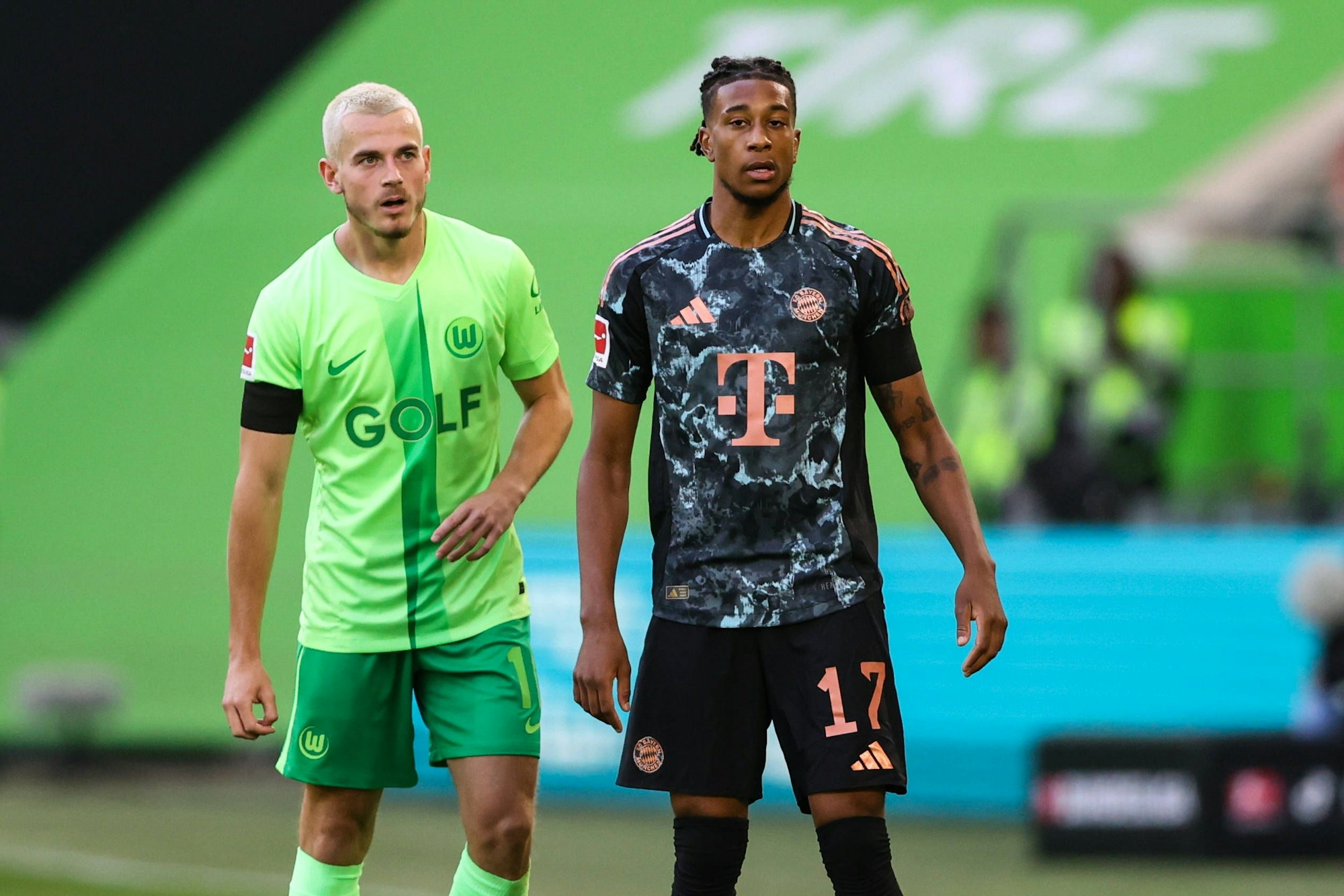 Jakub Kaminski und Michael Olise stehen beim Spiel des VfL Wolfsburg gegen den FC Bayern nebeneinander auf dem Platz.