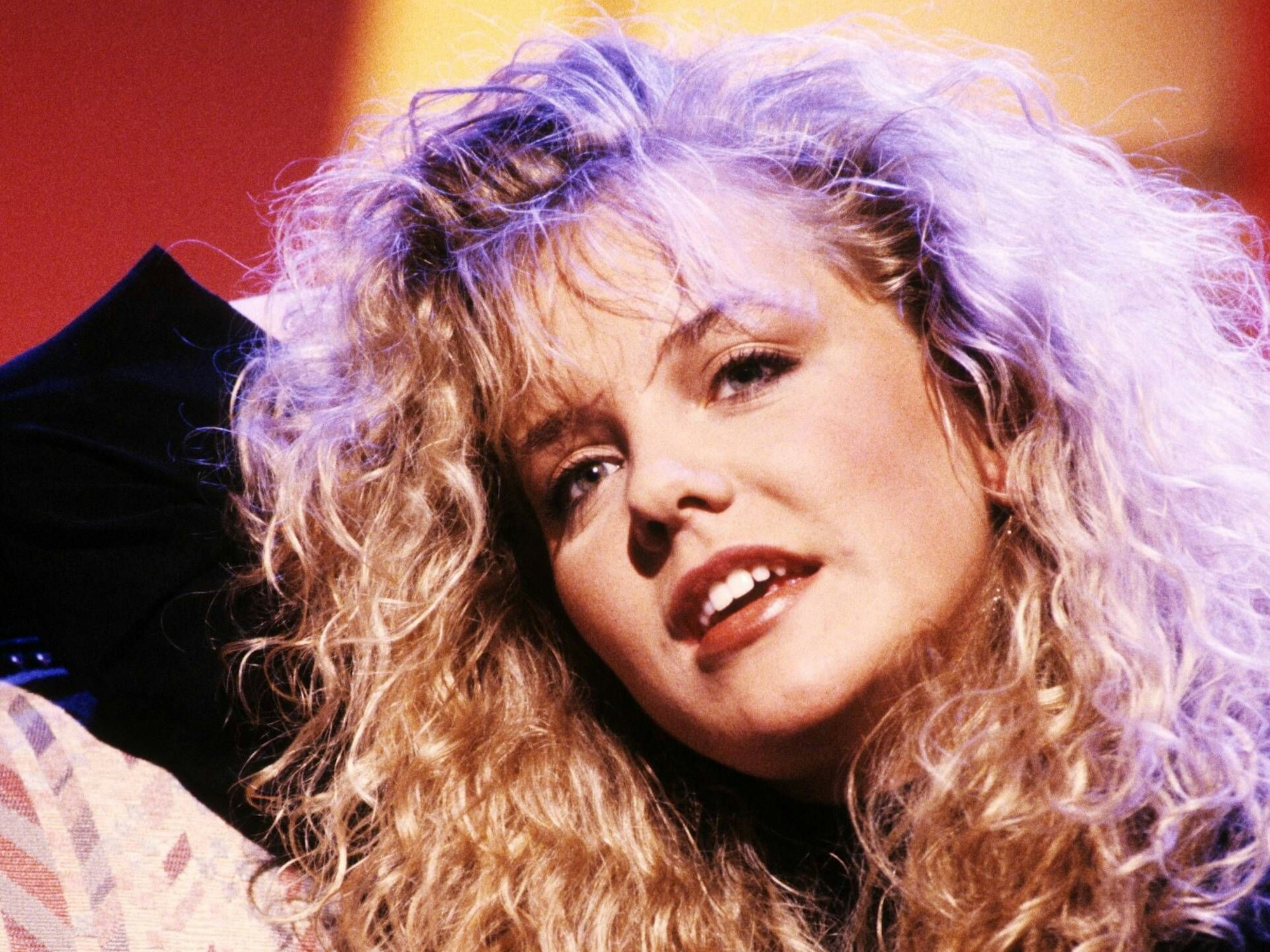 Inka Bause hält den Kopf schräg und lächelt in die Kamera, sie hat lange, lockige Haare.