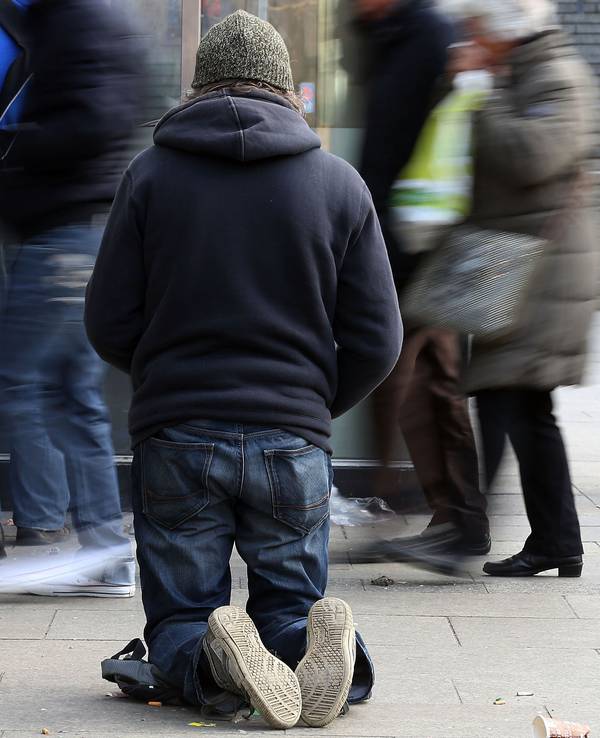 Ein Bettler kniet auf einem Gehweg.
