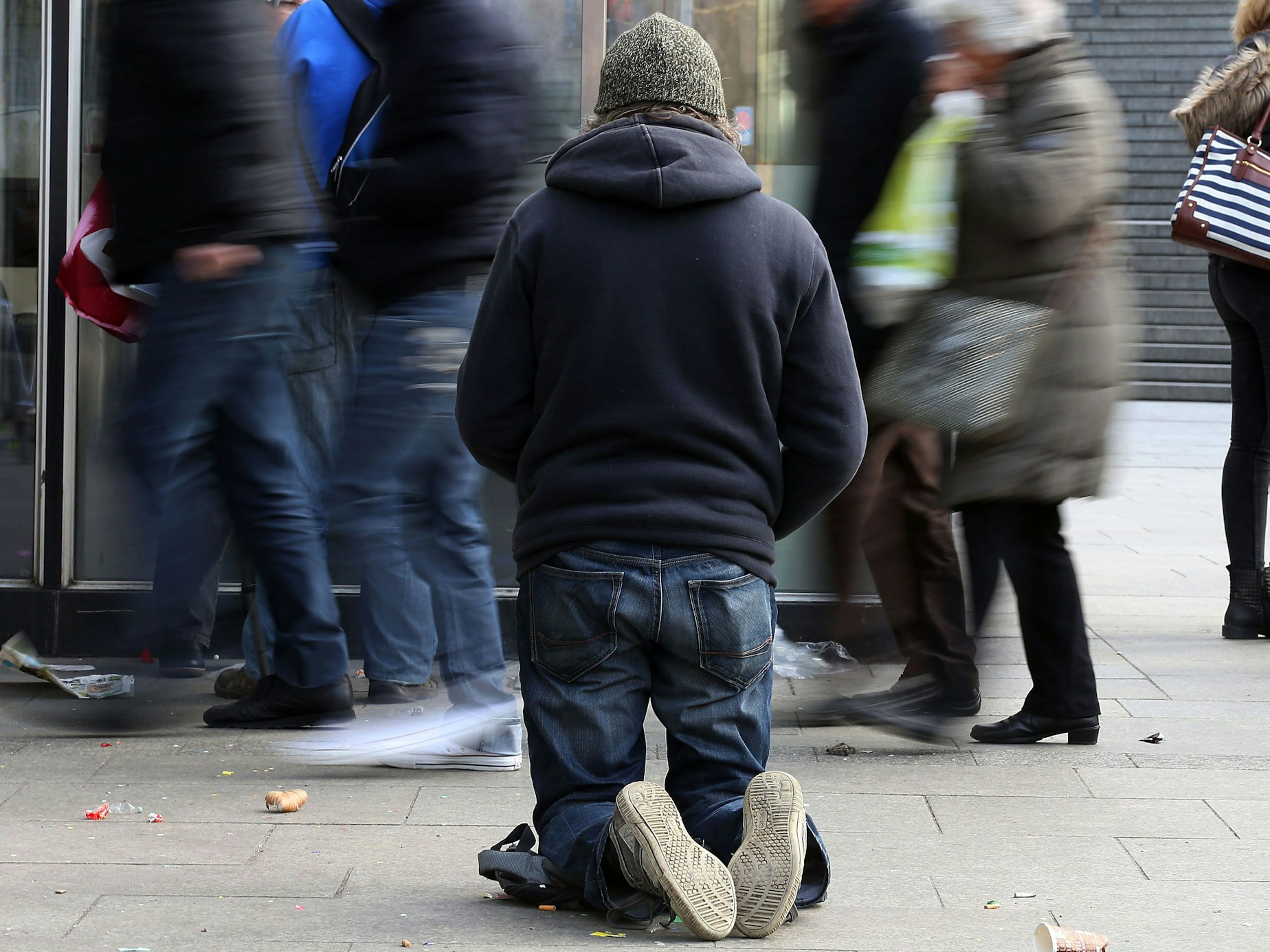Ein Bettler kniet auf einem Gehweg.