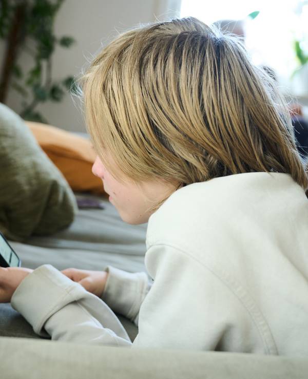 Ein Junge liegt auf einem Sofa und guckt auf sein Smartphone (gestellte Szene).