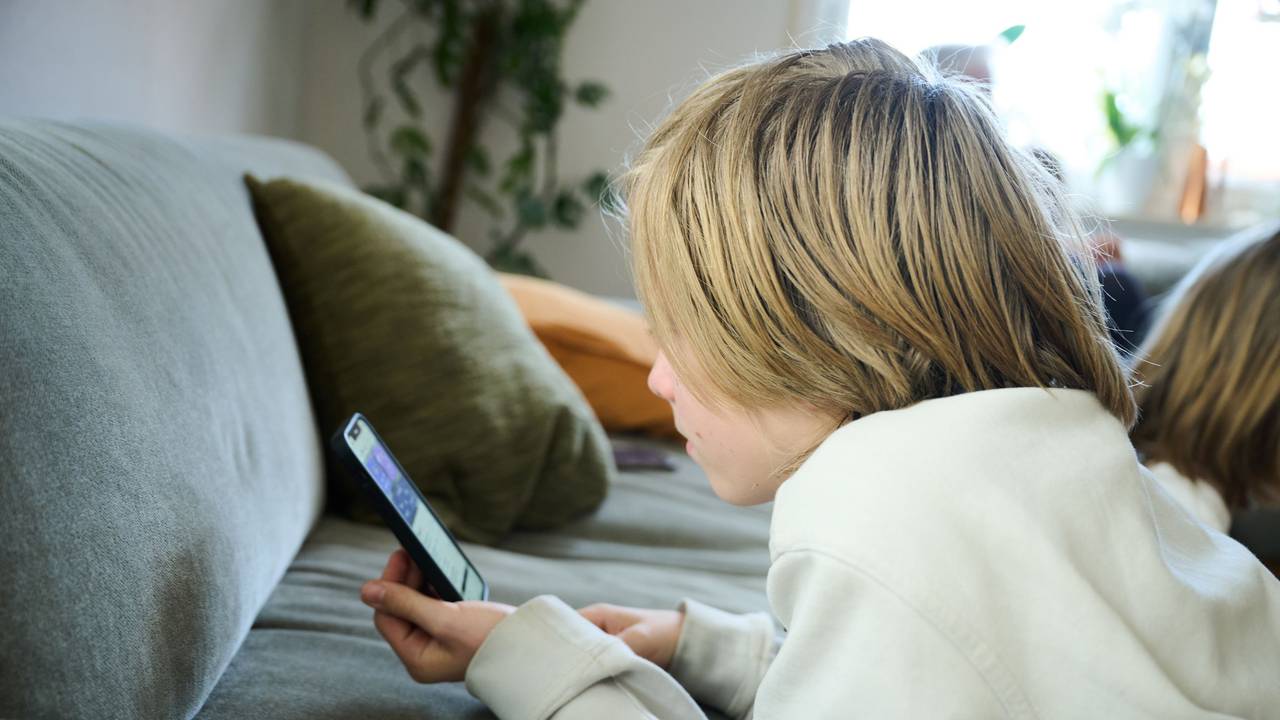 Ein Junge liegt auf einem Sofa und guckt auf sein Smartphone (gestellte Szene).