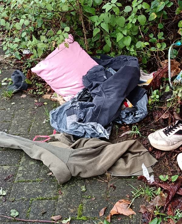 Kleidung und Schuhe liegen an einer Mauer auf der Erde.