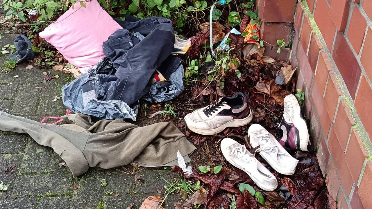 Kleidung und Schuhe liegen an einer Mauer auf der Erde.