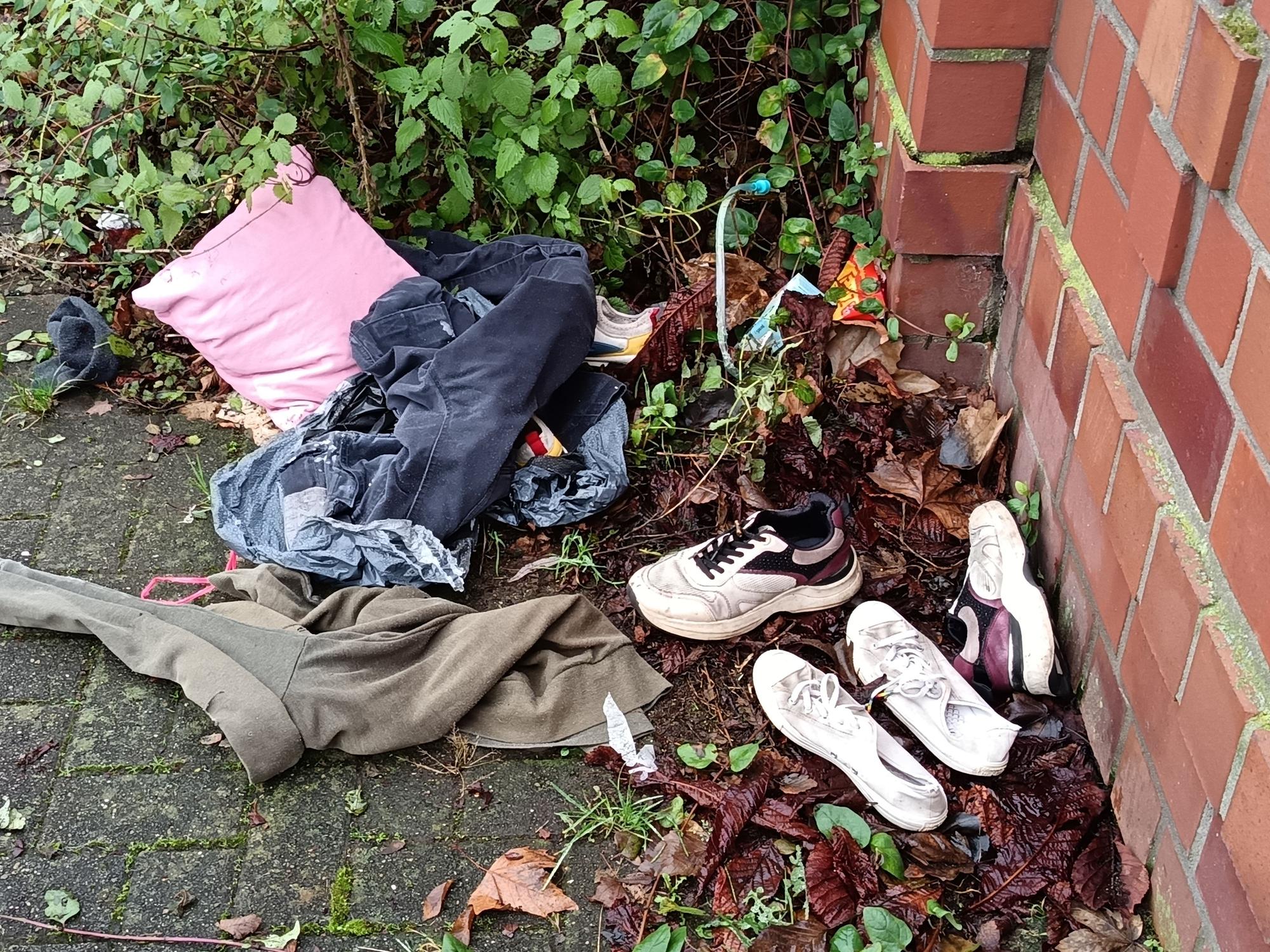 Kleidung und Schuhe liegen an einer Mauer auf der Erde.