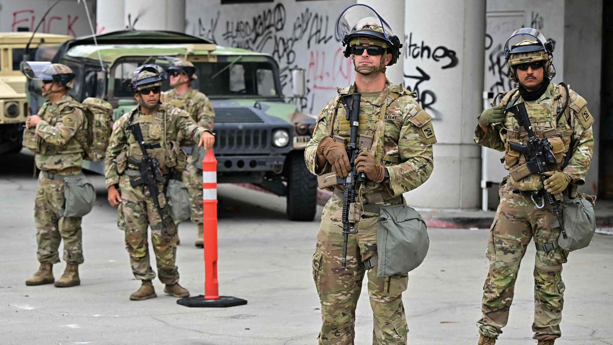 Fünf schwer bewaffnete Soldaten stehen vor einem Gebäude.