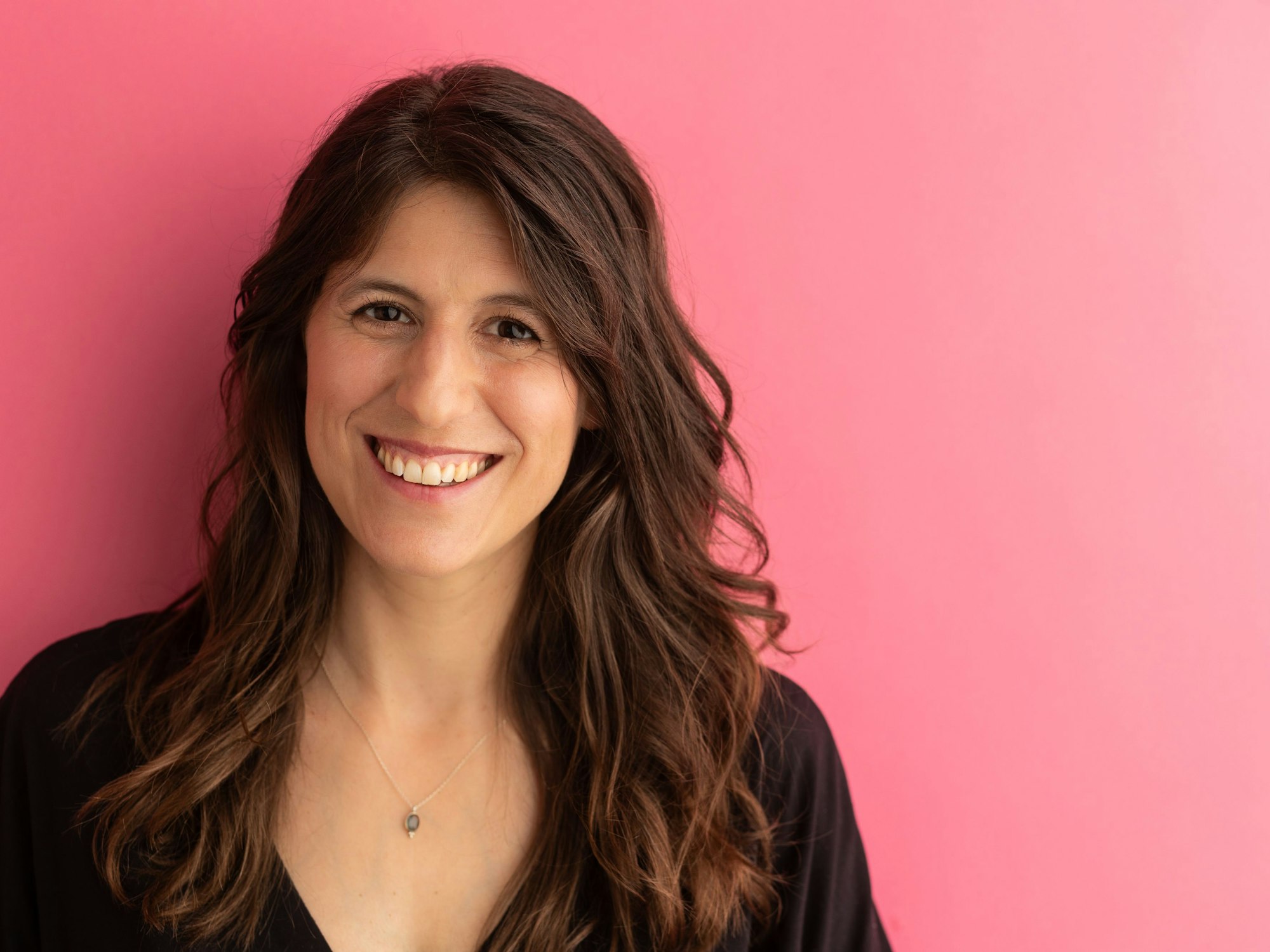 Die Ärztin Eva Mirasol lächelt freundlich vor einem pinken Hintergrund.