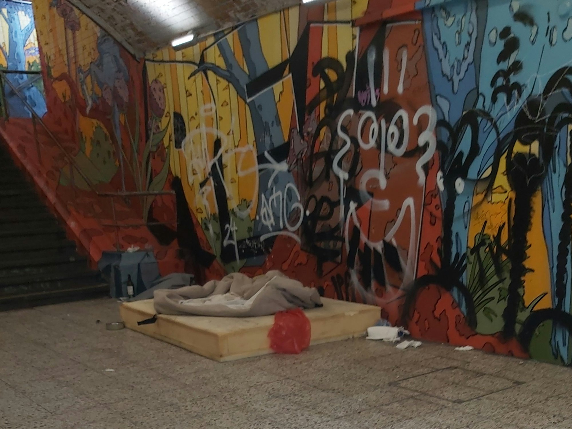 Eine Matratze neben einer Treppe an einer Bahnhaltestelle.