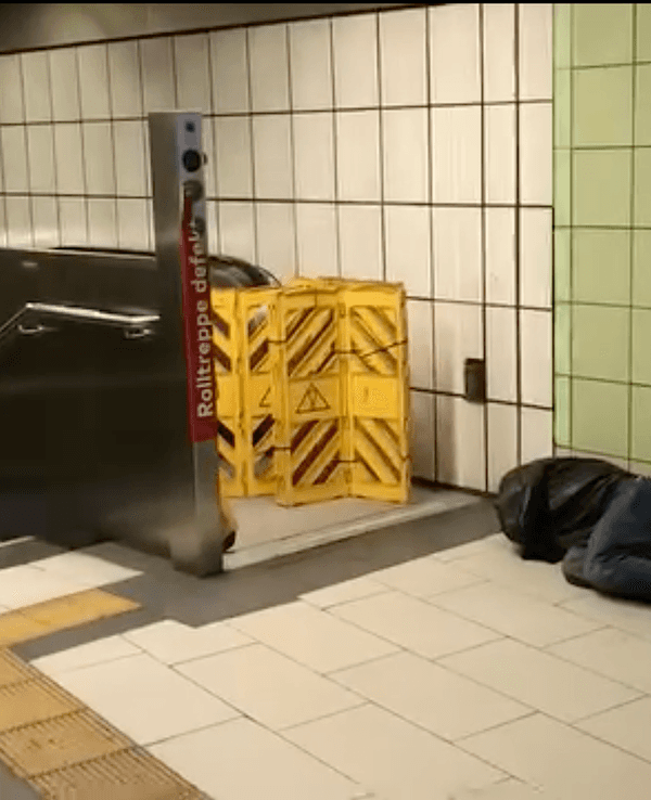 Ein Obdachloser schläft vor einer Rolltreppe an einer Haltestelle in Köln.