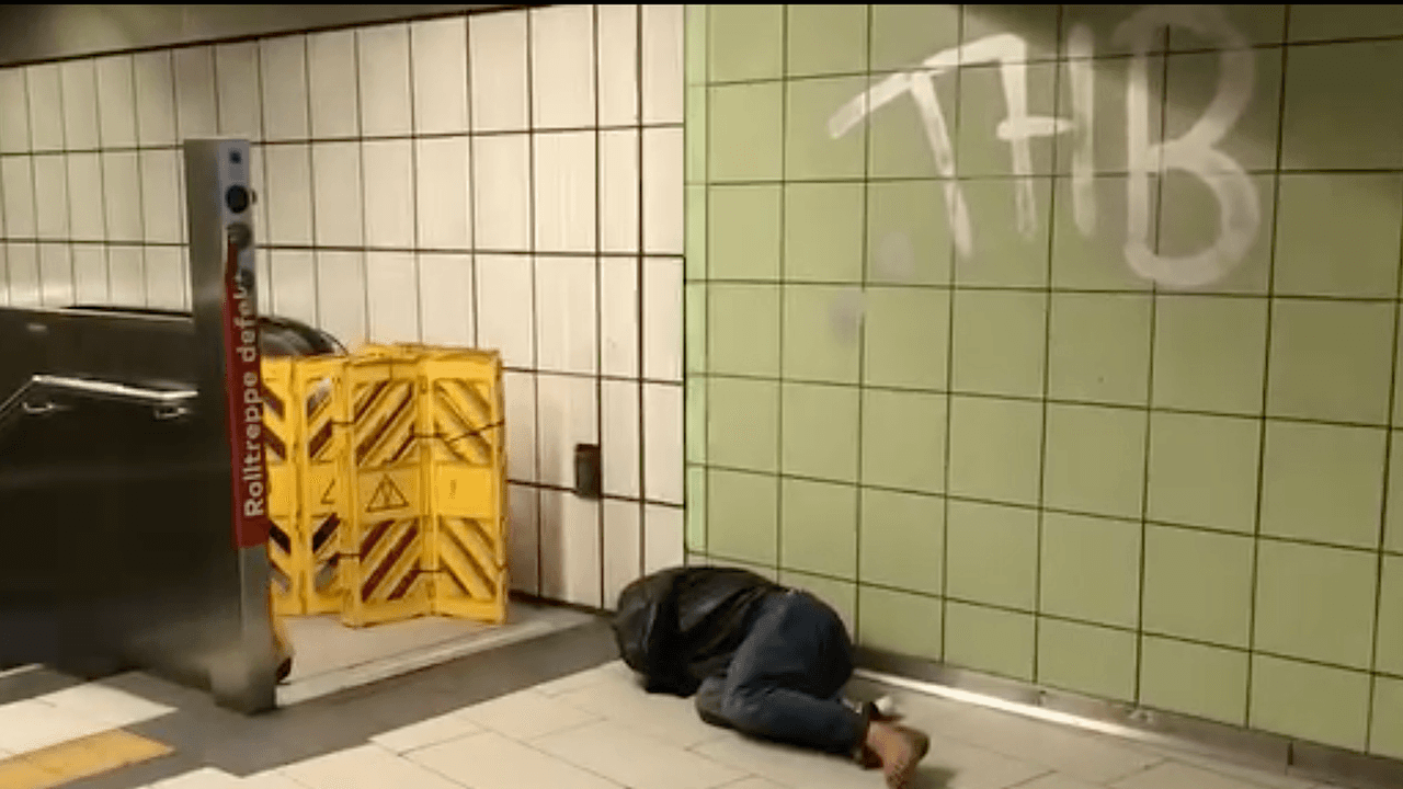 Ein Obdachloser schläft vor einer Rolltreppe an einer Haltestelle in Köln.