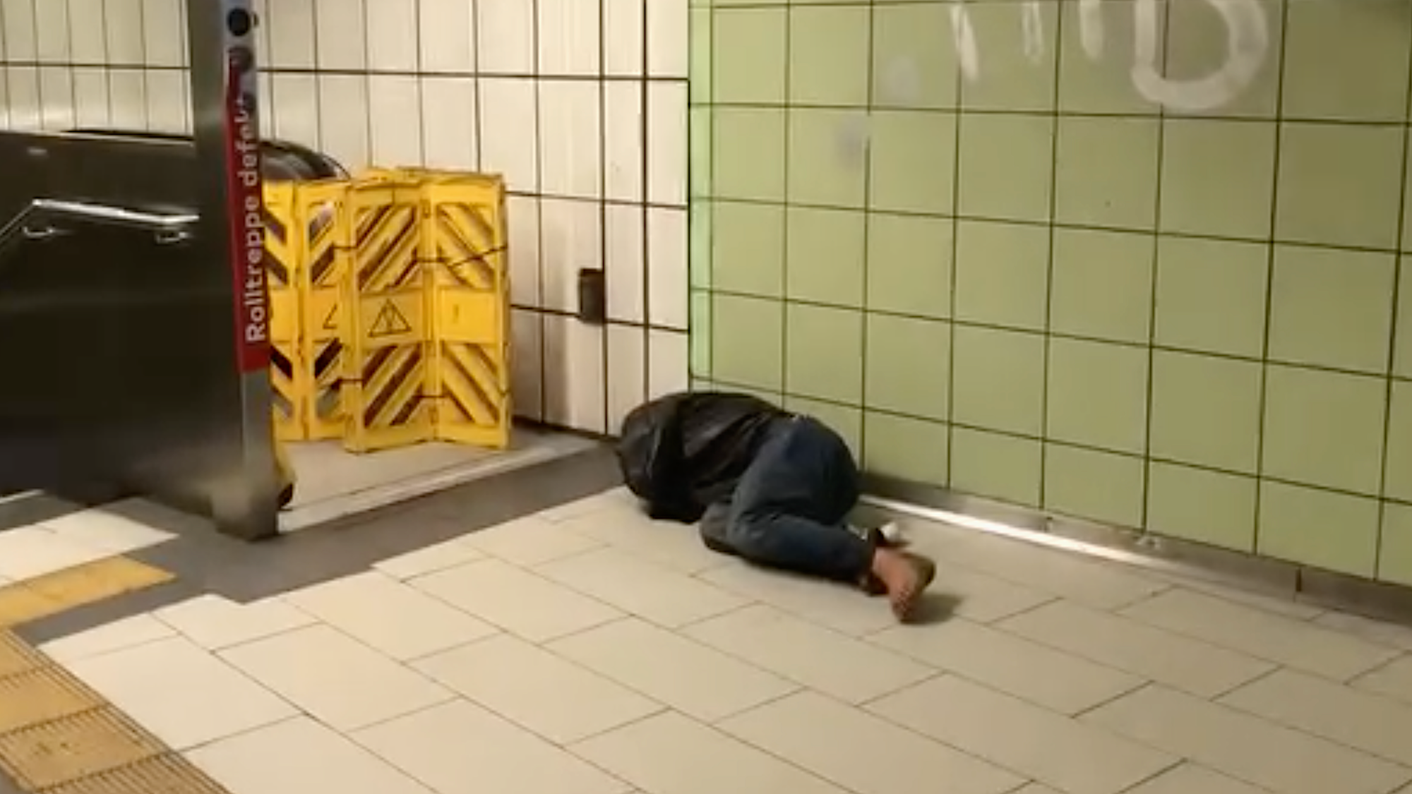 Ein Obdachloser schläft vor einer Rolltreppe an einer Haltestelle in Köln.