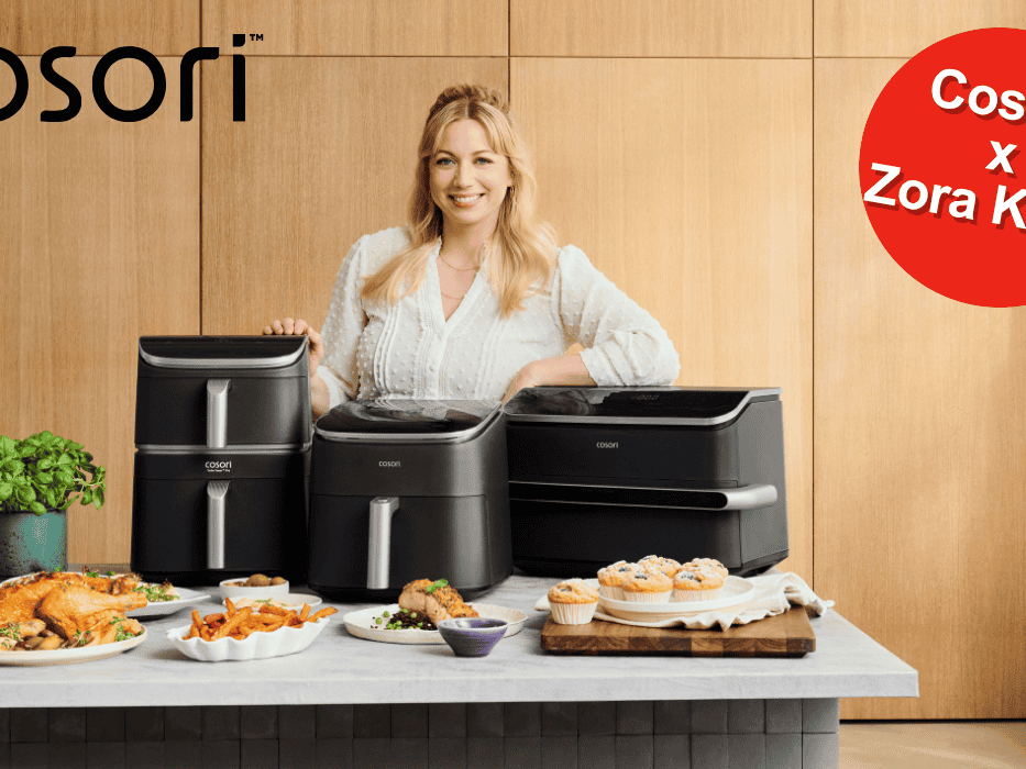 TV-Köchin Zora Klipp lächelnd hinter drei verschiedenen Cosori Heißluftfritteusen, umgeben von frisch zubereiteten Gerichten wie Hähnchen, Pommes und Muffins.