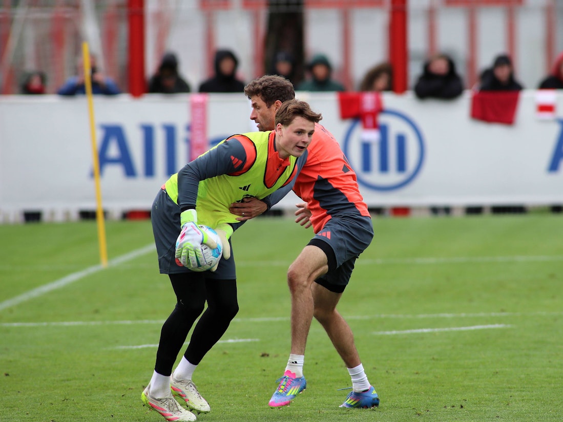Jonas Urbig fängt im Training den Ball, wird dabei leicht von Thomas Müller gestört.