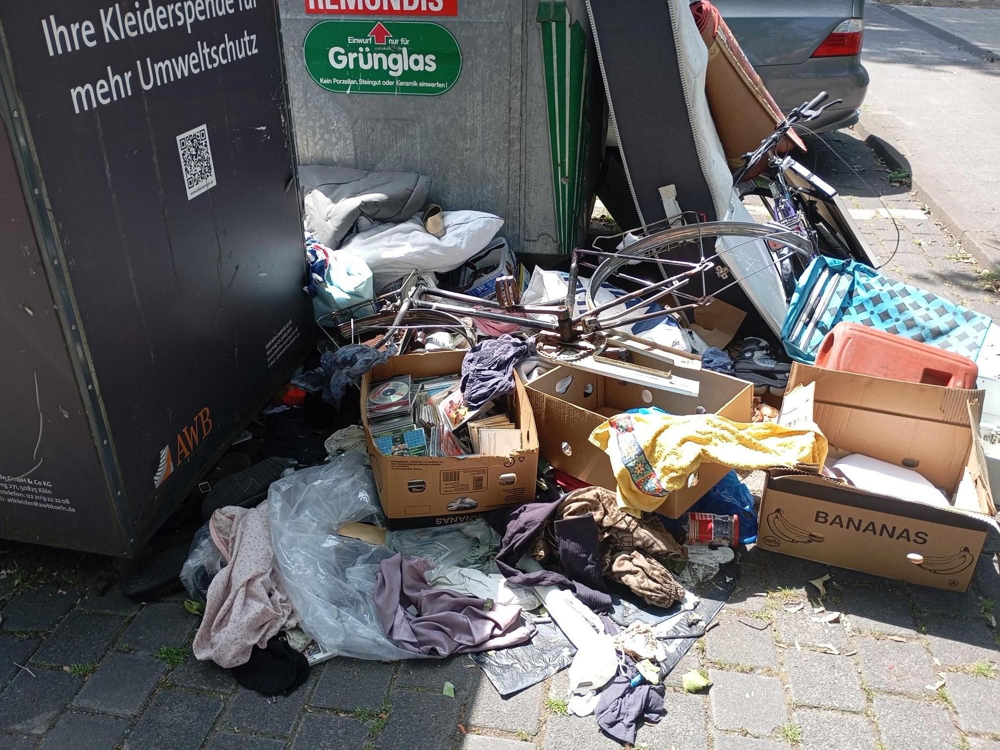 Vor Altkleider- und Glascontainern liegen Wäschestücke, eine Kiste mit CDs und Fahrräder ohne Reifen rum.