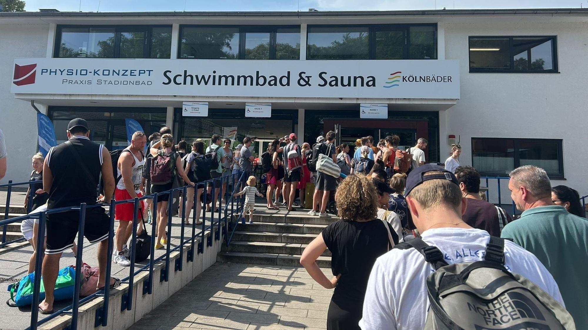 Vor einem Schwimmbad warten zahlreiche Menschen.