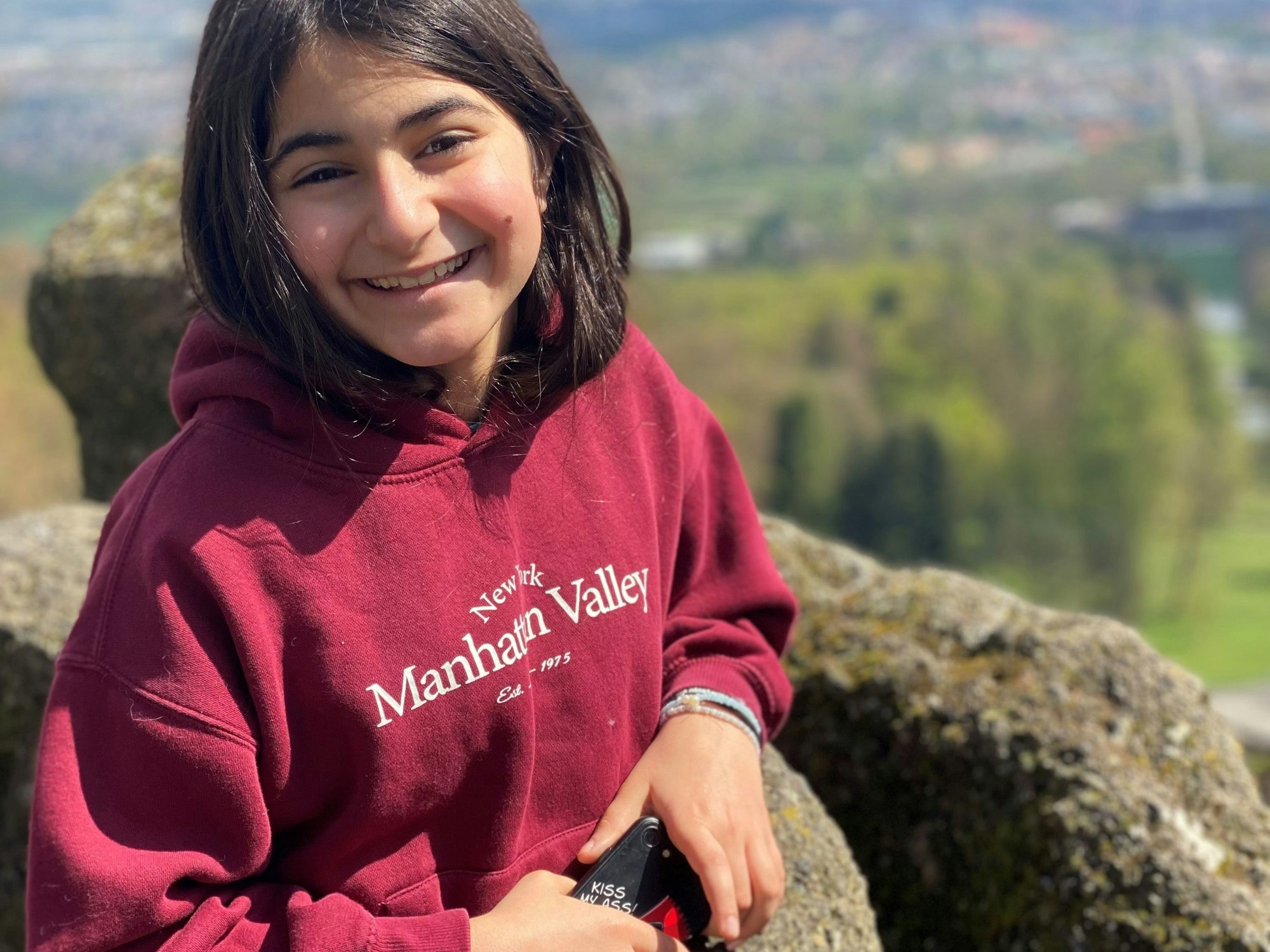 Ein Mädchen steht an einer Steinmauer.