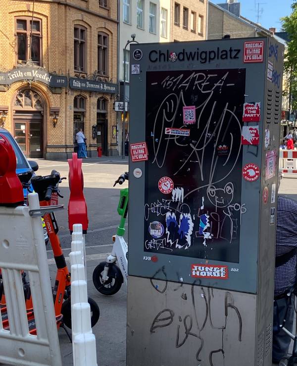 Eine Infosäule an einer Straße ist beschmiert und mit Aufklebern beklebt.