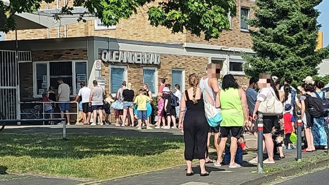 Leichtbekleidete Menschen stehen vor einem Schwimmbad Schlange.