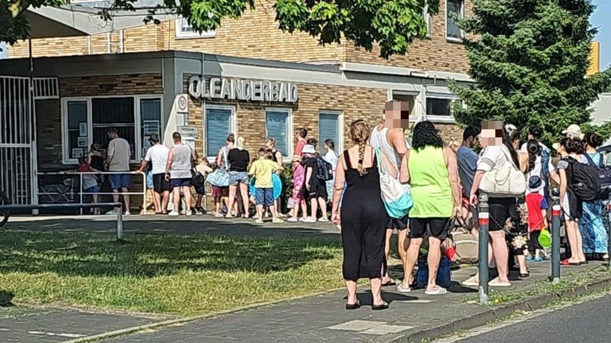 Leichtbekleidete Menschen stehen vor einem Schwimmbad Schlange.