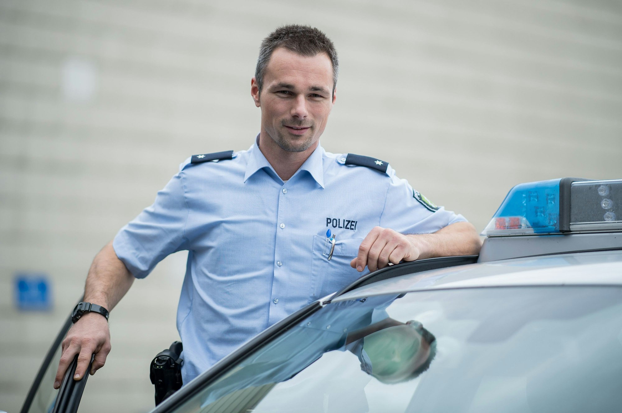 Dennis Eilhoff posiert in Polizeiuniform neben einem Streifenwagen.