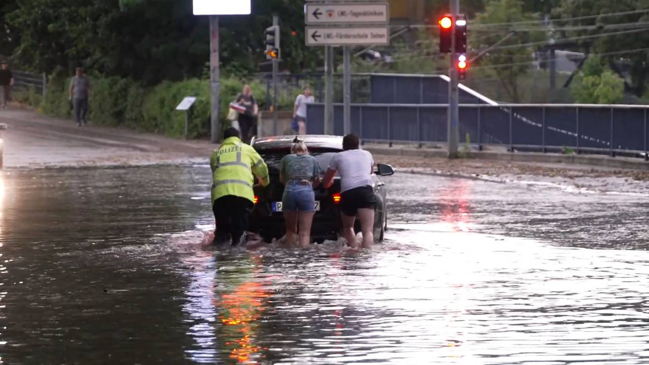 Menschen schieben ein Auto durch eine überflutete Straße. Ein schweres Unwetter hat am frühen Samstagabend große Teile des Kreisgebiets Paderborn getroffen.