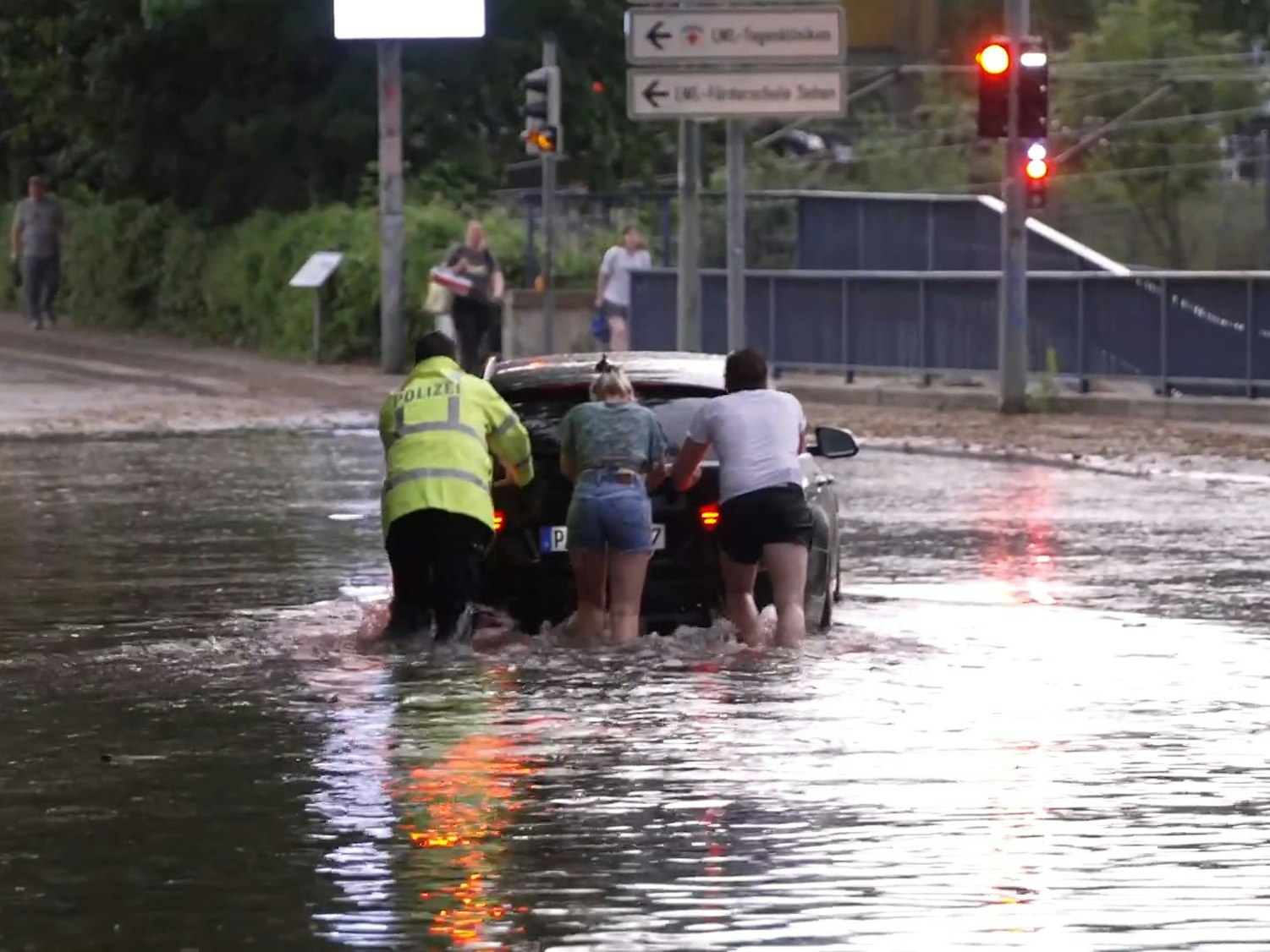 Menschen schieben ein Auto durch eine überflutete Straße. Ein schweres Unwetter hat am frühen Samstagabend große Teile des Kreisgebiets Paderborn getroffen.