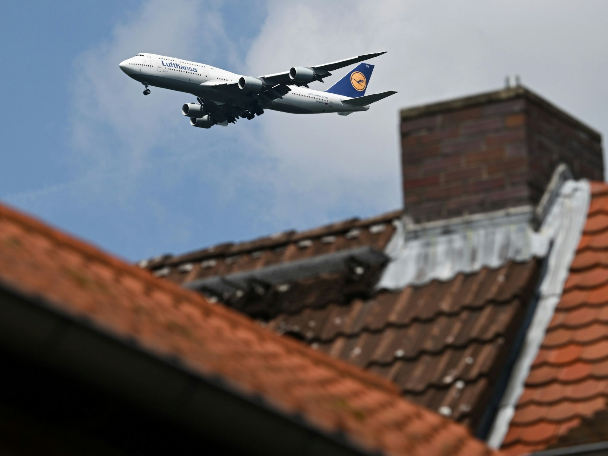 Eine Boeing 747-830 der Lufthansa ist hinter einem Haus im Landeanflug auf den Frankfurter Flughafen.