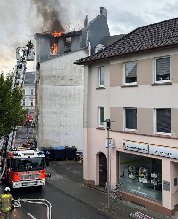 Flammen schlagen aus dem Dach eines mehrstöckigen Hauses, die Feuerwehr hat die Drehleiter ausgefahren.